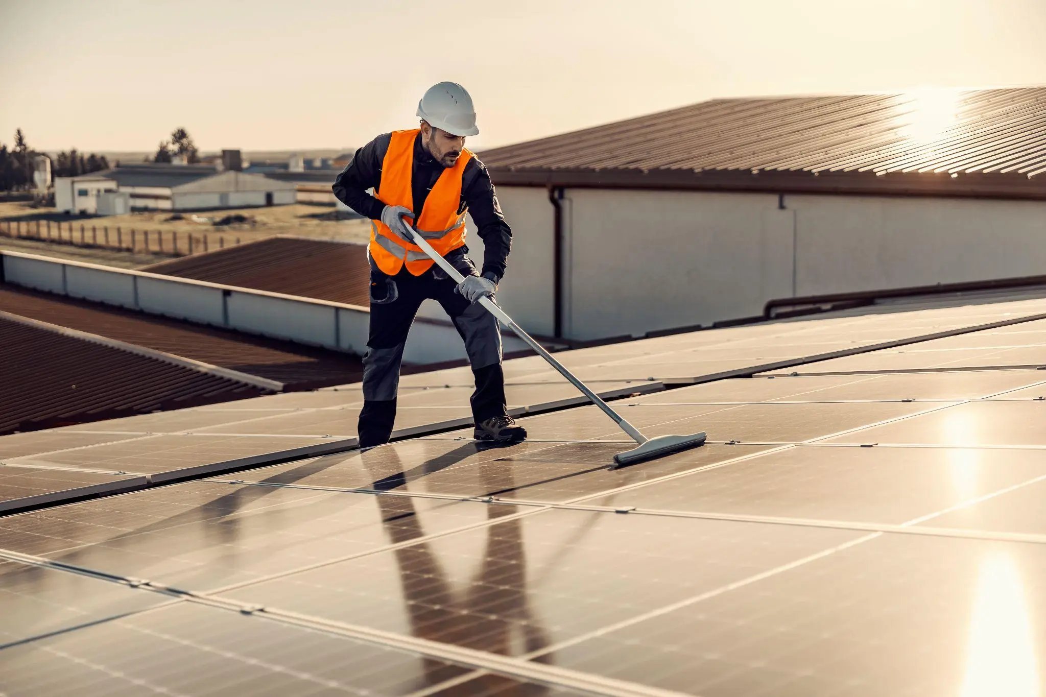a worker brooming solar panels on the roof at sunset