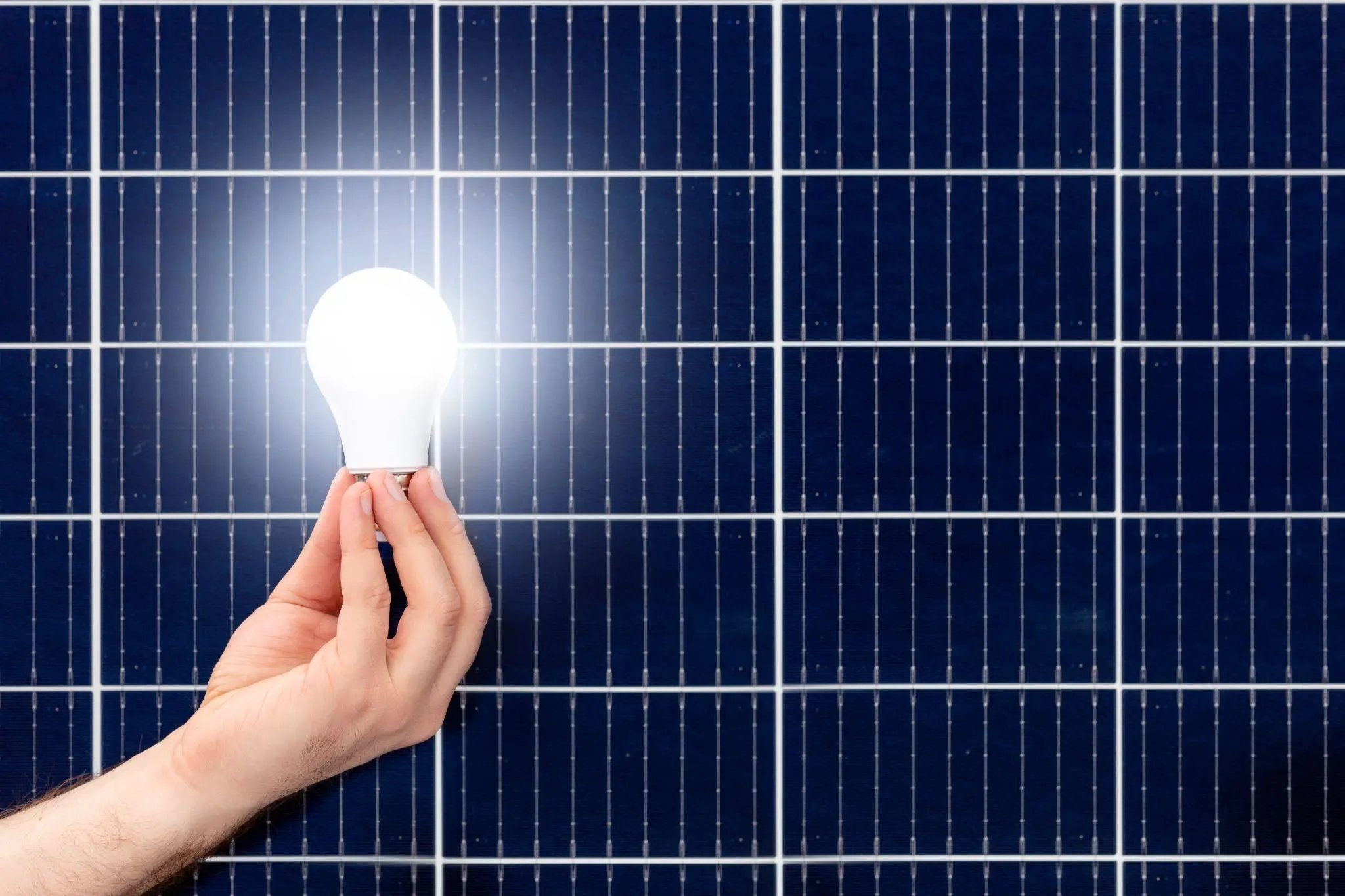 Hand holding white light bulb against solar panel, solar station. Idea concept of alternative energy, technology, environment, ecology. Green power energy.